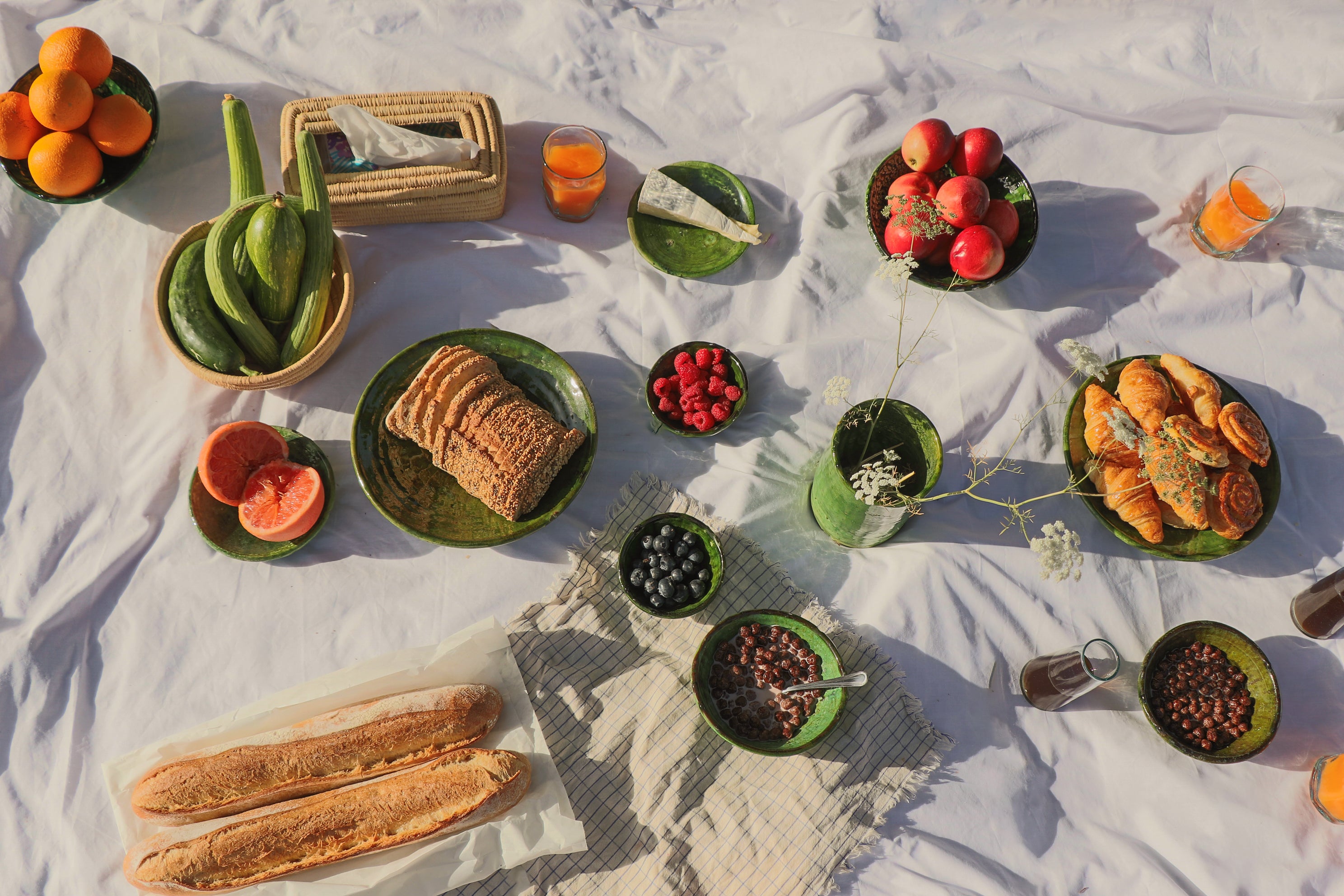 Moroccan outdoor breakfast spread styled with Tamegroute green glaze handmade ceramics and raffia, filled with fresh fruit, bread and pastries